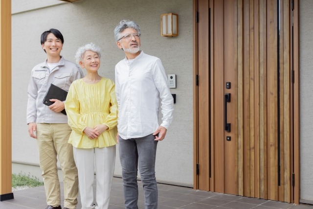 住宅の前に立つシニア夫婦と男性作業員